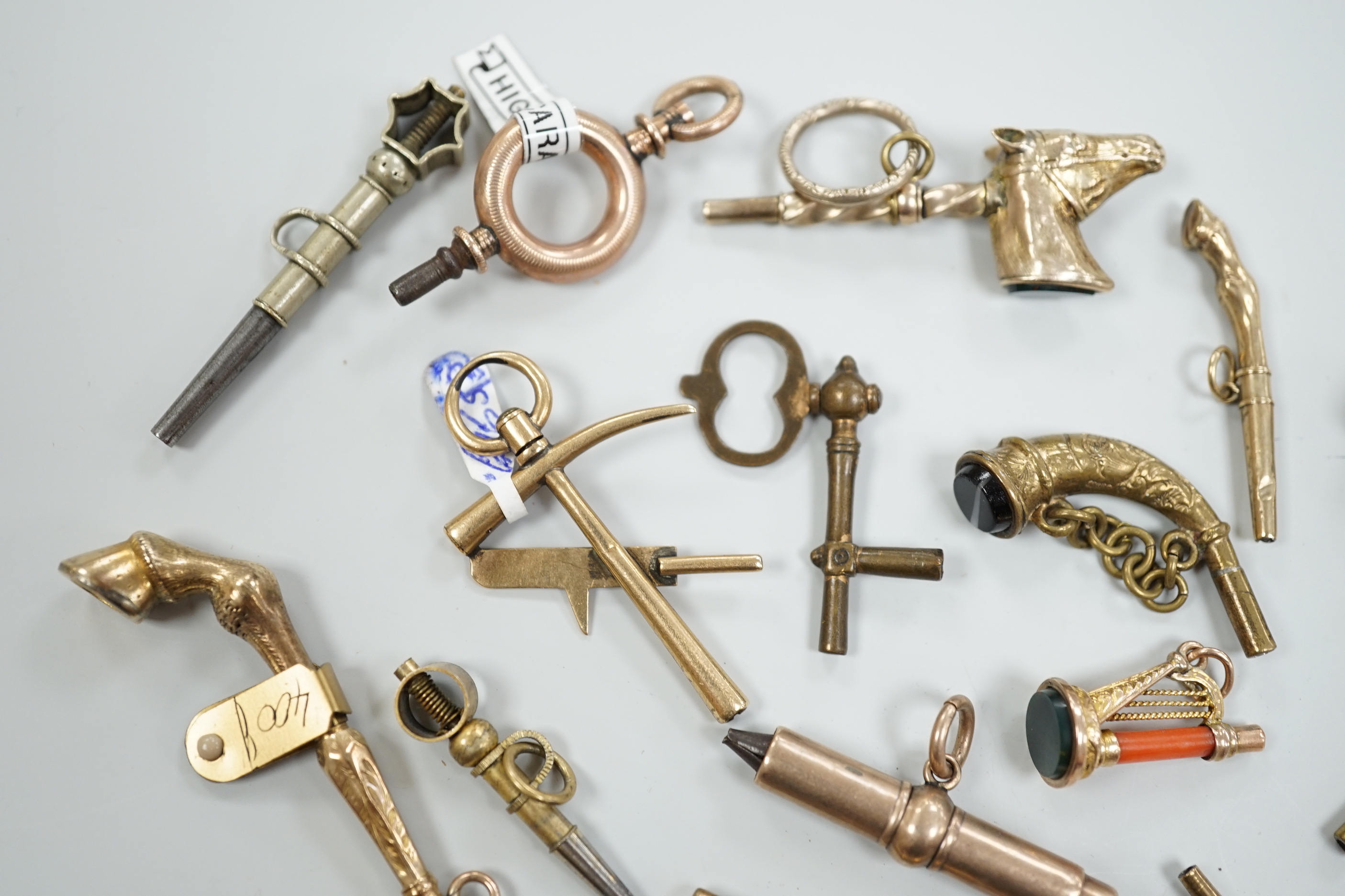 Eighteen assorted mainly 19th century base or yellow metal overlaid novelty watch keys, including coral and bloodstone set harp, pistol, rifle, cornucopia, bellows, horses hoof and trade insignia, largest 55mm.